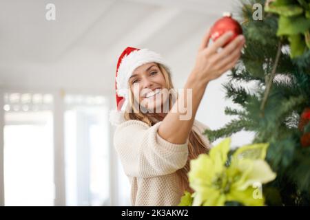 Entrer dans l'esprit de Noël. Une femme attrayante décorant son arbre de noël pendant qu'elle est à la maison. Banque D'Images