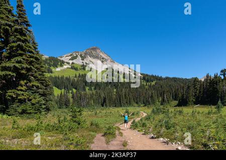 Femme marchant le long d'un sentier dans le parc provincial Garibaldi pendant une belle journée d'été avec Black Tusk Mountain en arrière-plan. Banque D'Images