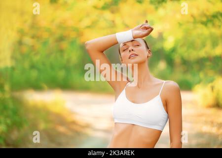 Épuisé mais se sentant super. Une femme essuyant la transpiration de son front pendant qu'elle est dehors pour un jogging dans le parc. Banque D'Images