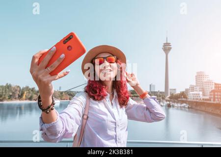 Happy girl Travel Blogger prend des photos de selfie sur son smartphone de la célèbre tour de télévision de Dusseldorf depuis le canal de Media Harbour dans la post-industrielle Banque D'Images