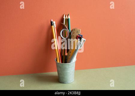 Porte-crayons sur bureau kaki. Fond mural rouge. Espace de travail, fournitures de bureau Banque D'Images