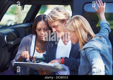Paillage sur une carte. Portrait d'un groupe d'amis se penchant contre leur camionnette, lisant une carte. Banque D'Images
