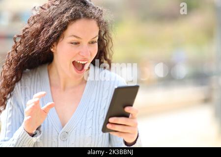 Une femme excitée qui s'est réjouite de regarder des nouvelles incroyables sur un smartphone dans la rue Banque D'Images