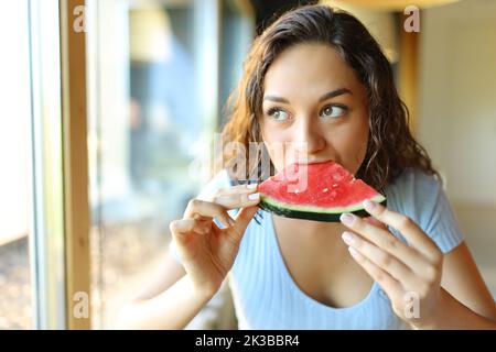 Femme dans un restaurant mangeant de pastèque regardant par une fenêtre Banque D'Images