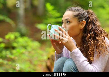 Femme buvant du café en regardant au-dessus dans une forêt Banque D'Images