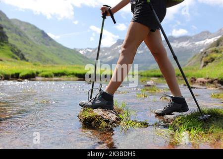 Gros plan d'un trekker jambes traversant la rivière marche avec des poteaux Banque D'Images