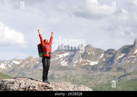 Portrait complet d'un randonneur en rouge levant les bras célébrant dans une haute montagne Banque D'Images