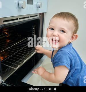 Bébé monte dans un four électrique chaud. Un enfant ouvre la porte du four dans la cuisine. Enfant d'un an Banque D'Images