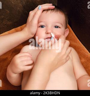 Une mère nettoie son nez avec un tampon en coton torsadé pour un bébé garçon heureux. Maman nettoie les narines d'un enfant souriant. Enfant d'un an Banque D'Images