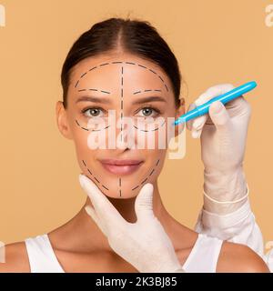 Le chirurgien en plastique dessine des marques sur le visage de la jeune femme pour une opération de chirurgie esthétique sur fond beige studio Banque D'Images