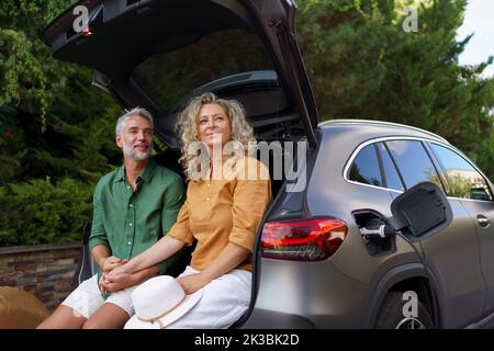 Couple d'âge moyen assis dans le coffre en attendant de charger la voiture avant de voyager pendant les vacances d'été. Banque D'Images