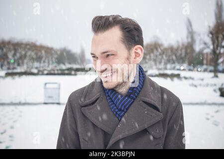 Portrait d'un jeune homme beau avec une barbe souriante en riant dans la neige d'hiver Banque D'Images