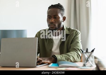Portrait d'un employé sérieux travaillant sur un ordinateur portable, assis au bureau à la maison, entrepreneur tapant sur le clavier Banque D'Images