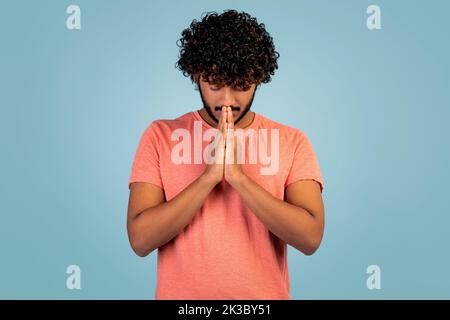 Jeune homme de l'est tenant les mains par la bouche, priant Banque D'Images