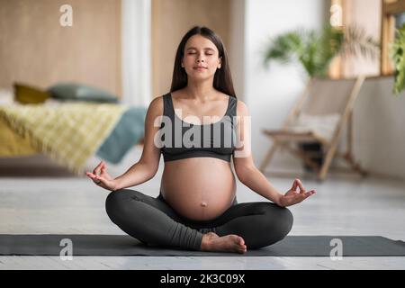Portrait de la jeune femme enceinte méditant sur le tapis de yoga à la maison Banque D'Images