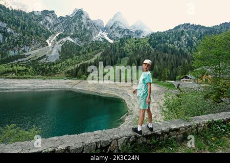 Garçon debout contre le lac et les montagnes à Vorderer Gosausee, Gosau, haute-Autriche. Banque D'Images