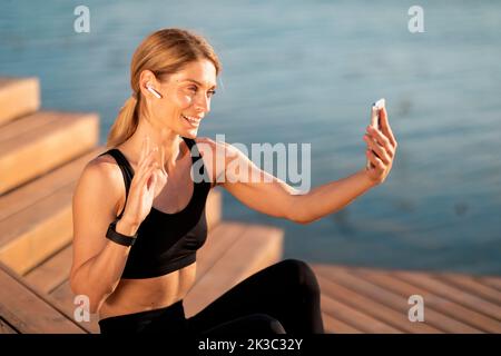 Femme sportive d'âge moyen effectuant un appel vidéo sur un smartphone pendant un entraînement en plein air Banque D'Images