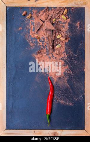 piments rouges et morceaux de chocolat noir sur fond noir Banque D'Images