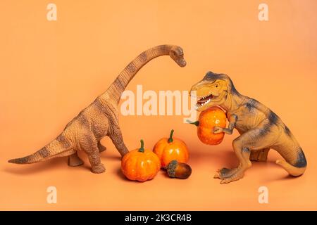 Jouet dinosaure Tyrannosaurus tenant la citrouille dans ses pattes, sur le podium blanc isolé sur fond orange carte de vœux de vacances Joyeux jour d'Halloween, Hello Autumn Creative minimal concept. Banque D'Images