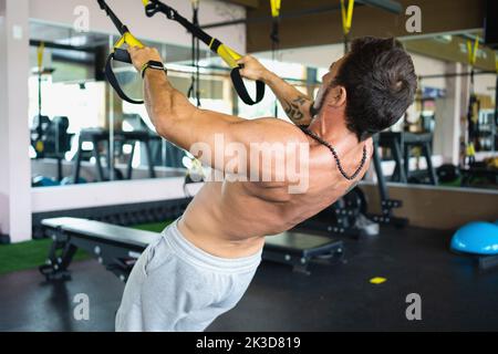 Vue arrière d'un homme fort s'exerçant avec trx dans une salle de gym Banque D'Images