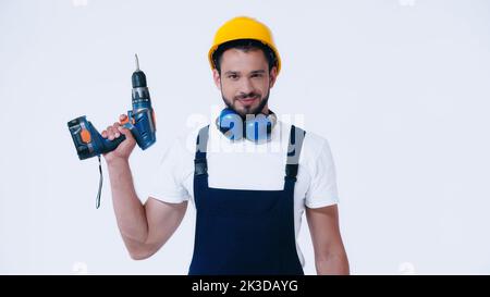 positif constructeur dans le casque et les combinaisons tenant la perceuse électrique et regardant la caméra isolée sur blanc, image de stock Banque D'Images