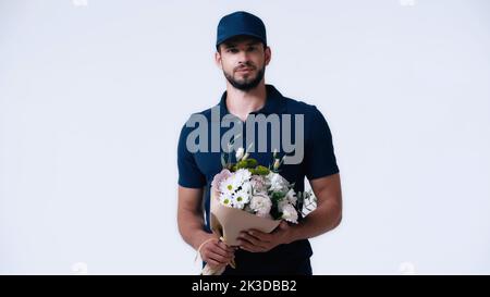jeune homme de livraison barbu avec bouquet regardant la caméra isolée sur blanc, image de stock Banque D'Images
