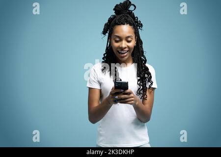 Une femme ethnique aux cheveux mauriques positifs utilise un téléphone portable vérifie les messages et lit les nouvelles tient le cellulaire moderne dans les mains regarde avec curieux heureux expression Banque D'Images