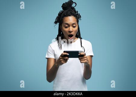 Une femme ethnique aux cheveux mauriques positifs utilise un téléphone portable vérifie les messages et lit les nouvelles tient le cellulaire moderne dans les mains regarde avec curieux heureux expression Banque D'Images