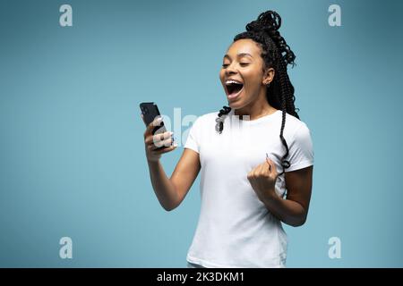 Une femme ethnique aux cheveux mauriques positifs utilise un téléphone portable vérifie les messages et lit les nouvelles tient le cellulaire moderne dans les mains regarde avec curieux heureux expression Banque D'Images