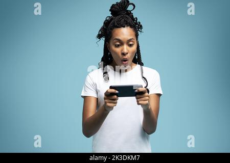 Une femme ethnique aux cheveux mauriques positifs utilise un téléphone portable vérifie les messages et lit les nouvelles tient le cellulaire moderne dans les mains regarde avec curieux heureux expression Banque D'Images