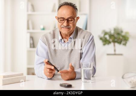 Homme mature assis à la maison et vérifiant le taux de sucre dans le sang avec le glucomètre Banque D'Images