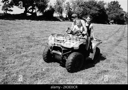 Agriculteur et deux garçons qui font du quad, High Bickington, North Devon, Angleterre, Royaume-Uni. Banque D'Images