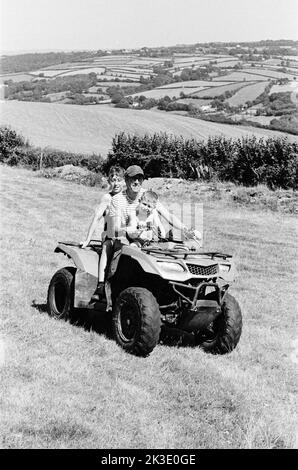 Agriculteur et deux garçons qui font du quad, High Bickington, North Devon, Angleterre, Royaume-Uni. Banque D'Images