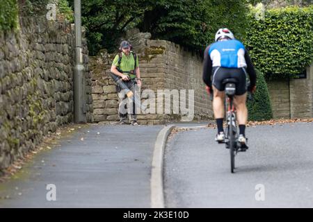 Homme utilisant un souffleur de feuilles portatif pour souffler les feuilles hors de l'arrière et hors de la manière d'un cycliste approchant, Royaume-Uni Banque D'Images