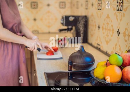 La femme prépare la nourriture à côté d'un diffuseur d'arôme. La cuisine coupe des poivrons rouges mûrs. Cuisson de salade de poivrons frais, mûrs pour les clients. Été Banque D'Images