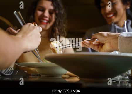 Groupe multiethnique de jeunes amis souriants mangeant des boulettes dim sum au bar-restaurant Fusion - gros plan sur les baguettes cueillant la nourriture - la nourriture et Banque D'Images