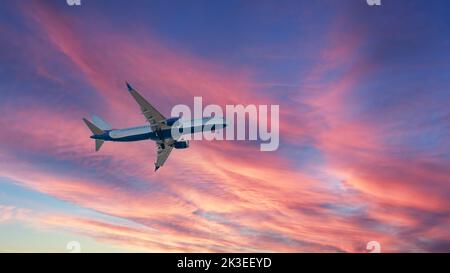 Un avion vole dans un coucher de soleil violet-rouge. Réglage du soleil. Coucher de soleil. Banque D'Images