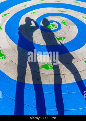 Ombres de couple contre la spirale bleue peinte sur la chaussée - Chatellerault, Vienne (86), France. Banque D'Images