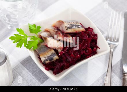Salade de hareng appétissante avec betteraves, crème sure et persil dans une assiette blanche Banque D'Images