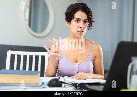 Belle jeune femme brune utilisant un ordinateur portable à la maison montrant et pointant vers le haut avec les doigts numéro quatre Banque D'Images