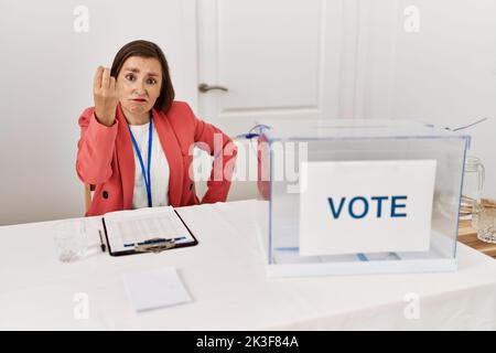 Belle femme hispanique d'âge moyen aux élections politiques, assise par bulletin de vote, faisant le geste italien avec la main et les doigts expression confiante Banque D'Images