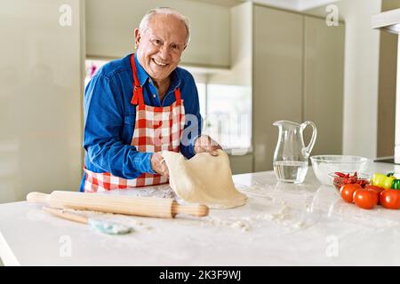 Homme âgé souriant confiant tenant la pâte avec les mains dans la cuisine Banque D'Images