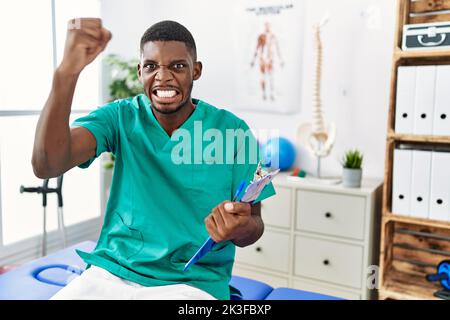 Un jeune afro-américain qui travaille à la clinique de rétablissement de la douleur est en colère et fou levant le poing frustré et furieux tout en criant avec colère. Rage et aggre Banque D'Images