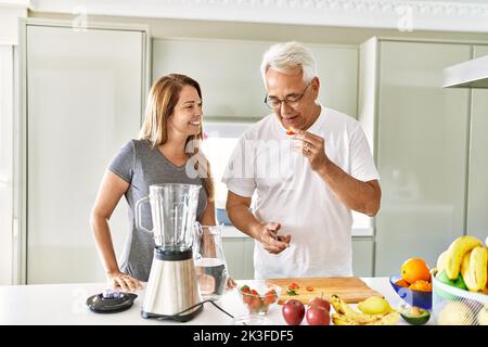 Couple hispanique d'âge moyen souriant smoothie à la cuisine. Banque D'Images