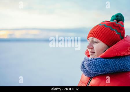 portrait d'une fille dans un chapeau rouge et un foulard riant dans une forêt enneigée par temps froid. Banque D'Images