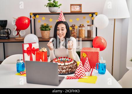 Femme hispanique célébrant l'anniversaire avec un grand gâteau au chocolat faisant appel vidéo criant fier, célébrant la victoire et le succès très excité avec élevé Banque D'Images