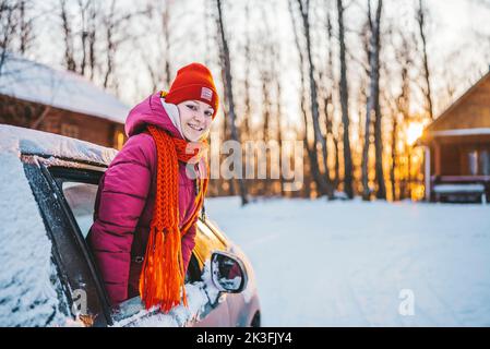 en hiver, une fille dans un chapeau rouge fait passer la main d'une voiture enneigée et rit par temps froid. Banque D'Images