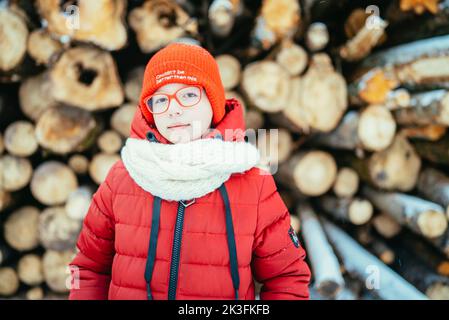 portrait d'une fille en hiver en lunettes sur fond de bois de chauffage par temps froid. Banque D'Images
