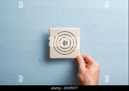 Main masculine plaçant un carreau de bois avec un symbole de cible dessiné dessus sur un fond en bois bleu pastel. Banque D'Images