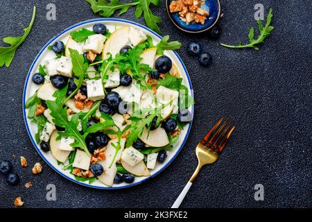 Delicious arugula salad with pears, blueberries, roquefort cheese and walnuts. Black kitchen table background, top view Banque D'Images